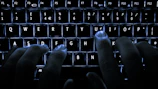Close-up of hands typing on a keyboard with a dark background and orange accents.
