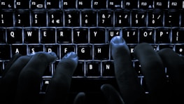 Hands typing on a sleek keyboard in a dimly lit room emphasizing focus and professionalism.