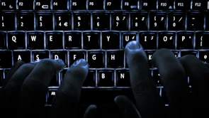 Close-up of hands typing on a keyboard with a dark background and orange accents.
