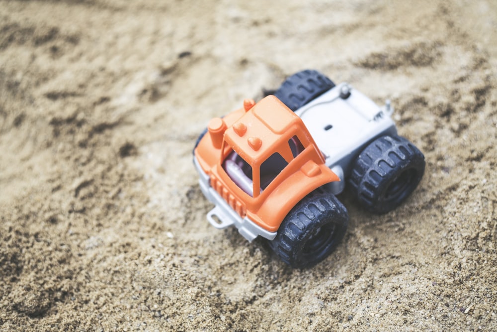 Fotografia de foco raso do brinquedo plástico do caminhão laranja na areia