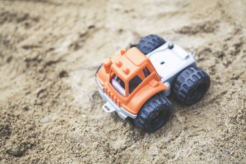 Flachfokusfotografie von orangefarbenem LKW-Plastikspielzeug auf Sand
