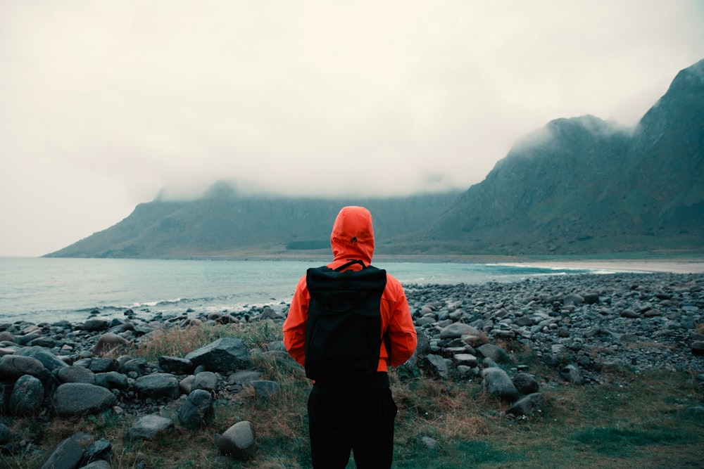 Persona con chaqueta con capucha naranja que lleva una bolsa mirando las montañas cubiertas de niebla