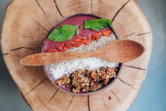 Close-up of a colorful smoothie bowl topped with fresh berries and mint leaves on a rustic wooden table.