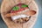A bowl filled with a smoothie is topped with vibrant ingredients such as mint leaves, chia seeds, goji berries, coconut shreds, and granola. It is presented on a wooden surface with a textured wooden spoon resting on top.
