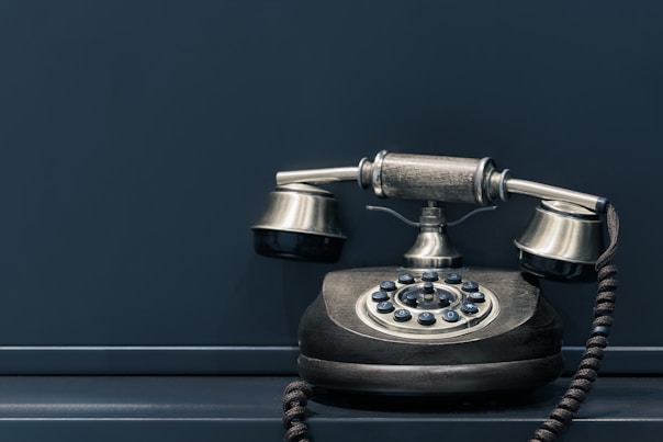 black and brown rotary phone near gray wall