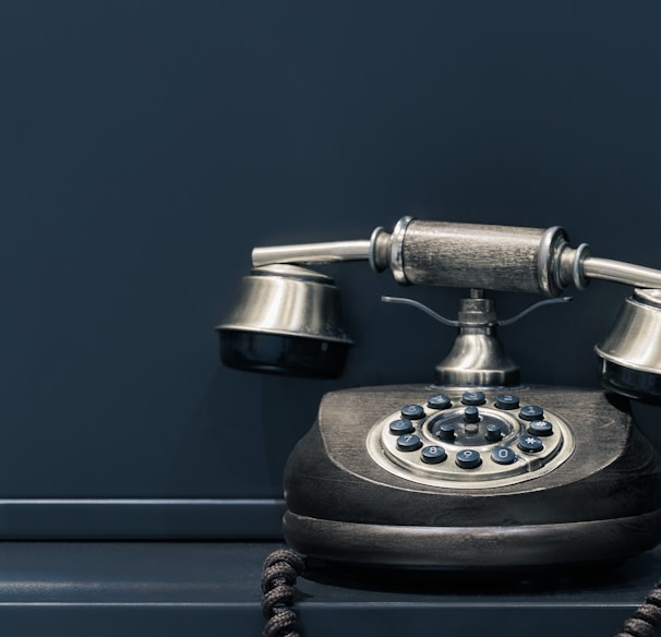 black and brown rotary phone near gray wall