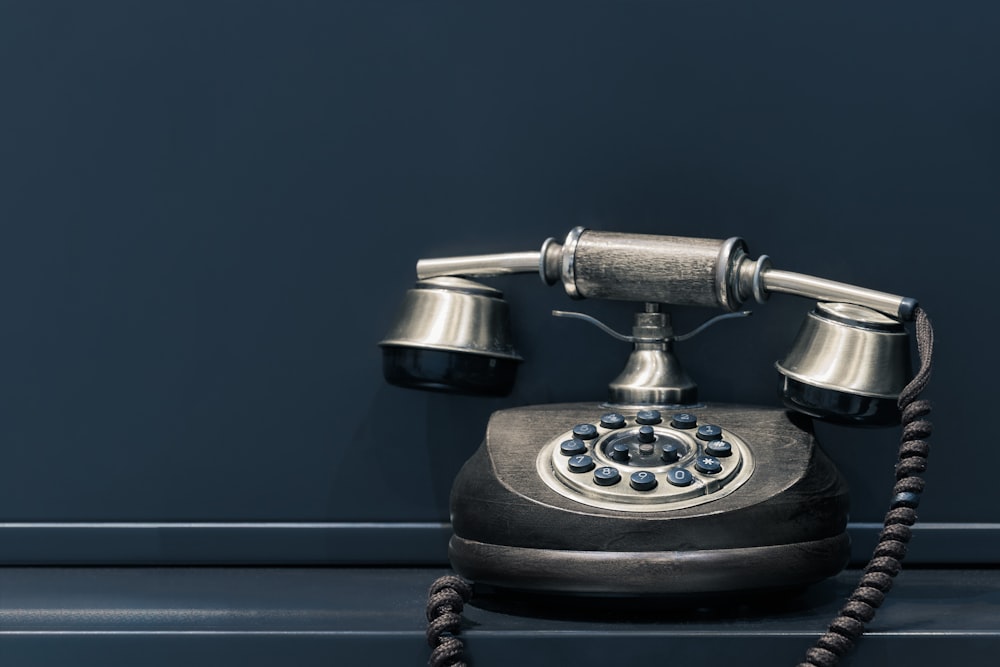 téléphone à cadran noir et marron près d’un mur gris