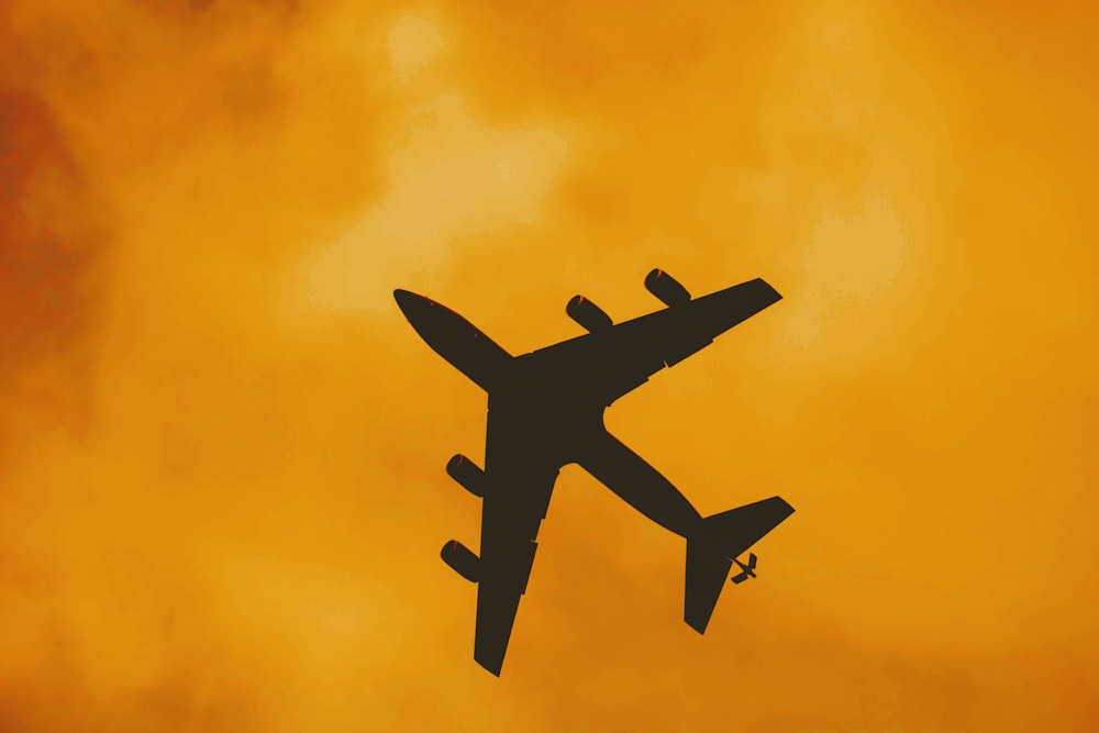 オレンジ色の曇り空に浮かぶ飛行機のシルエット
