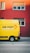 A bright yellow delivery van with the words 'DIE POST' in black and a red cross logo is parked on a street in front of a red building. The building has several windows with closed shutters.