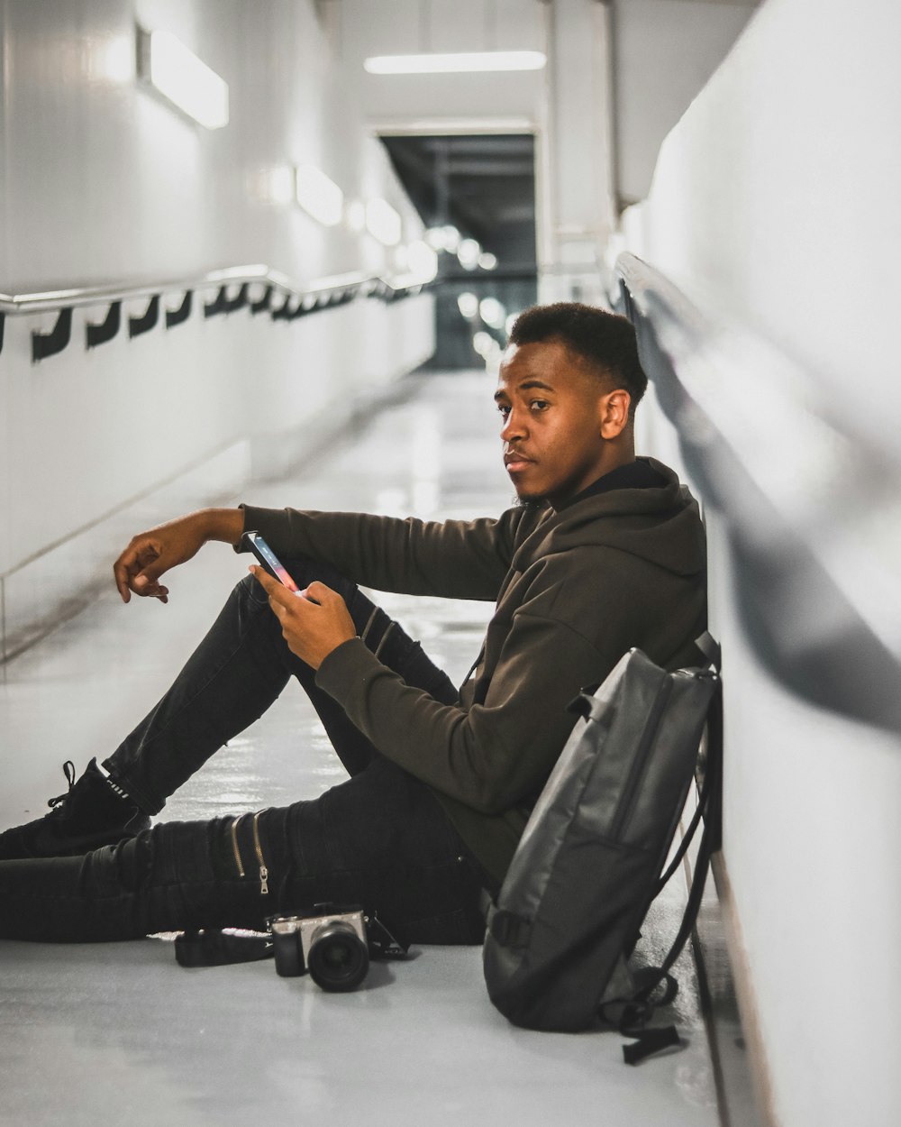 selective focus photography of man in jacket sitting on floor while holding smartphone