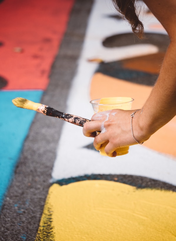 person holding cup with yellow paint and paintbrush