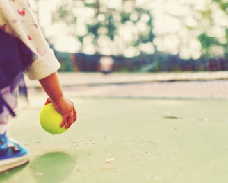 kid holding tennis ball in front of goal net