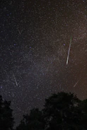 A night sky filled with streaks of bright meteors over a peaceful rural landscape