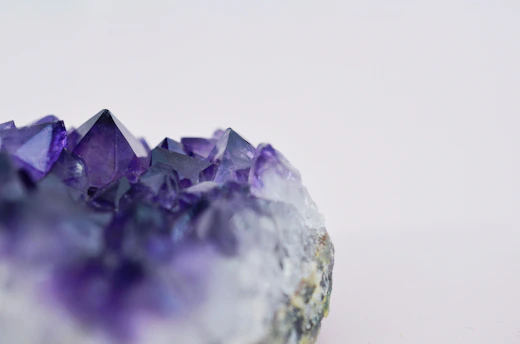 Close-up of a deep purple amethyst crystal cluster glowing softly against a white background.