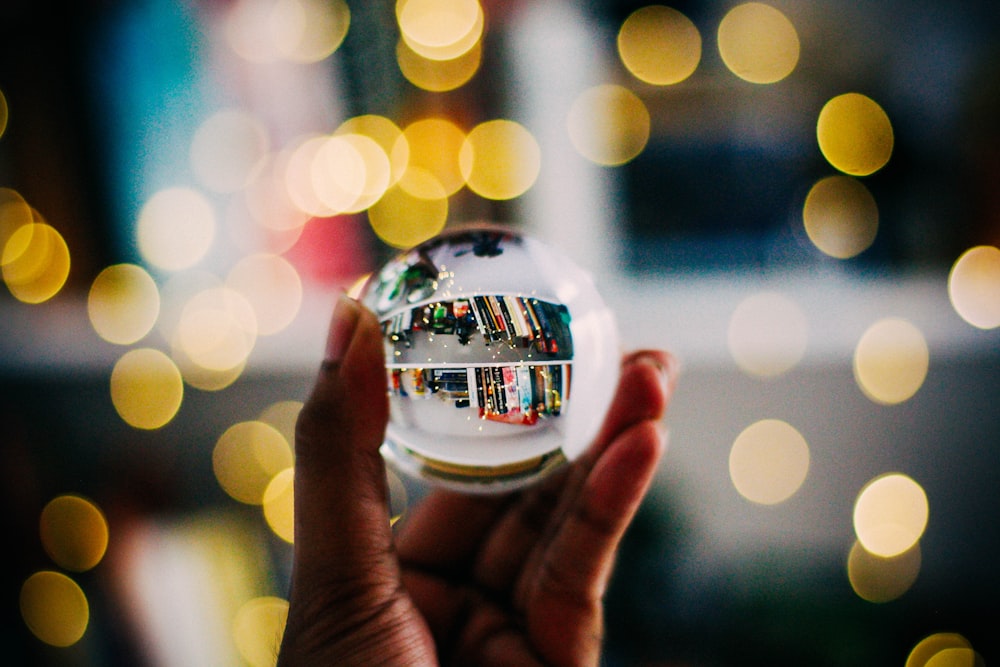 Persona sosteniendo una bola de cristal transparente con fotografía de fondo bokeh