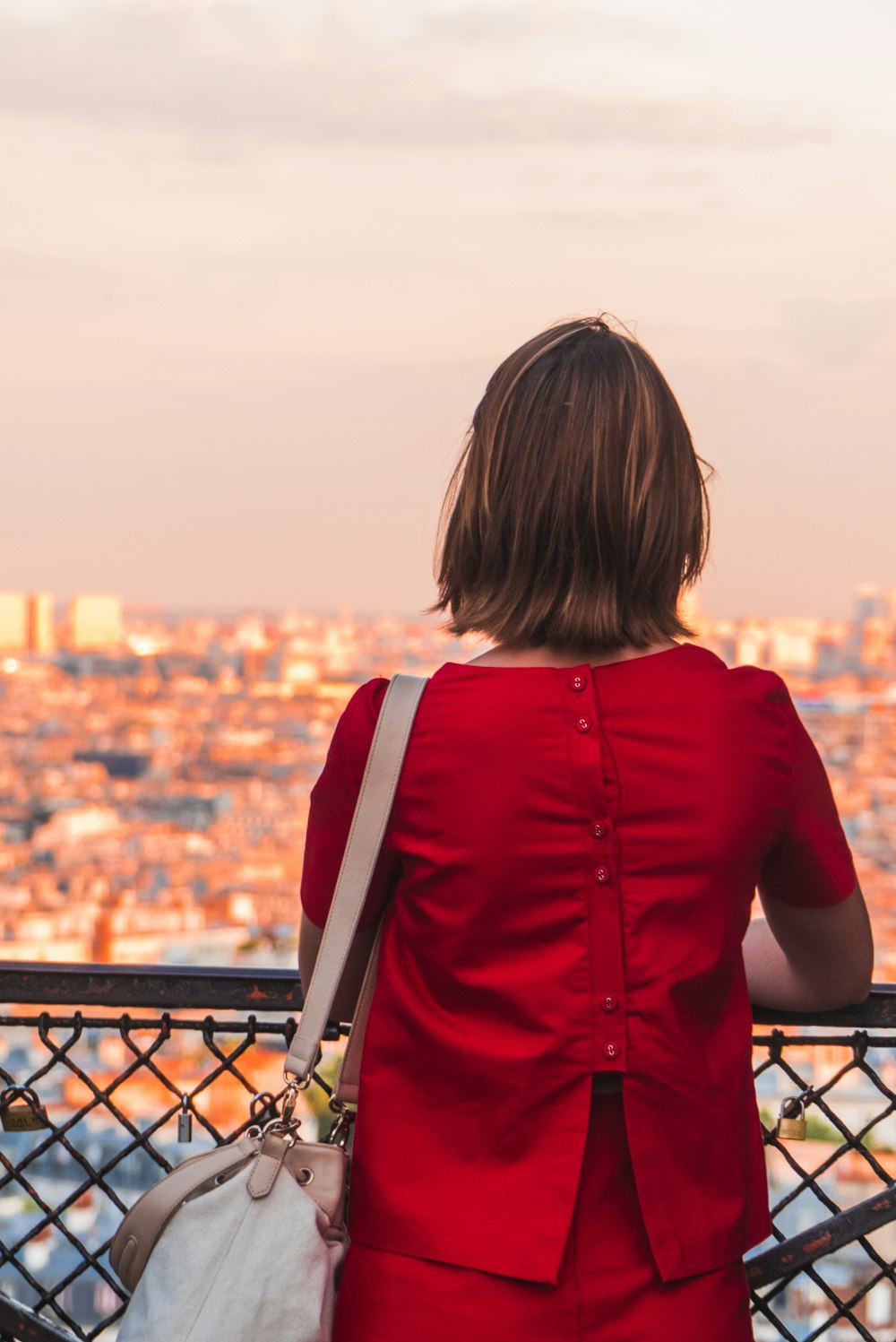 woman in red shirt and red bottoms outfit leaning on brown metal fence