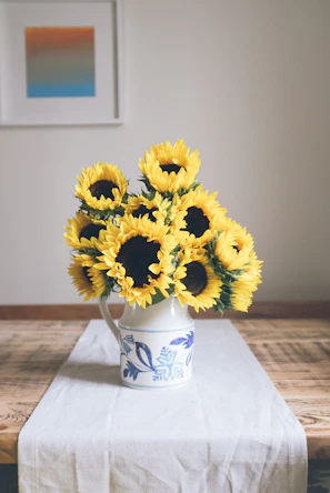A bright yellow ceramic pitcher filled with fresh wildflowers on a wooden table.