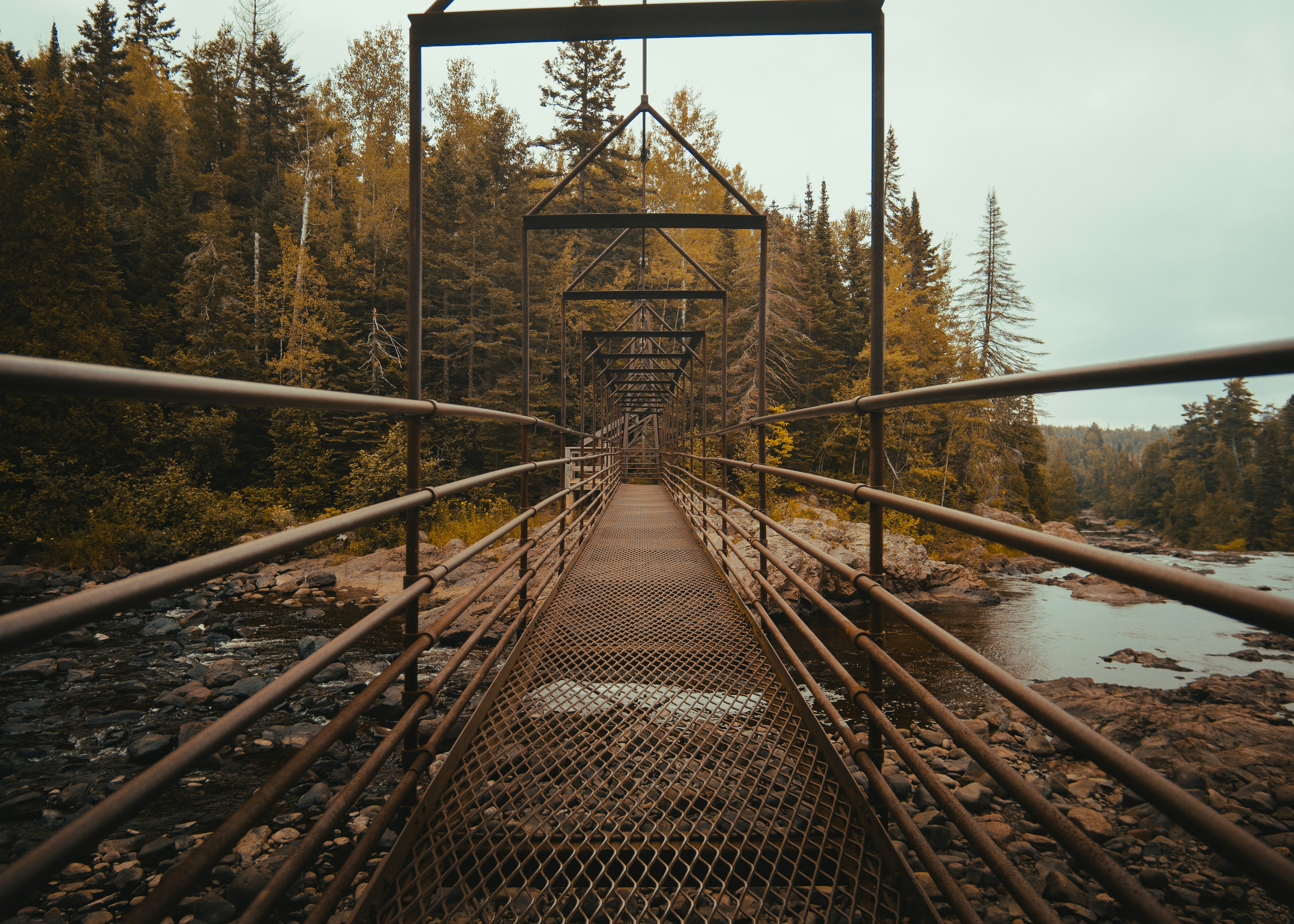 brown metal bridge above rocky river architectural photography at daytime
