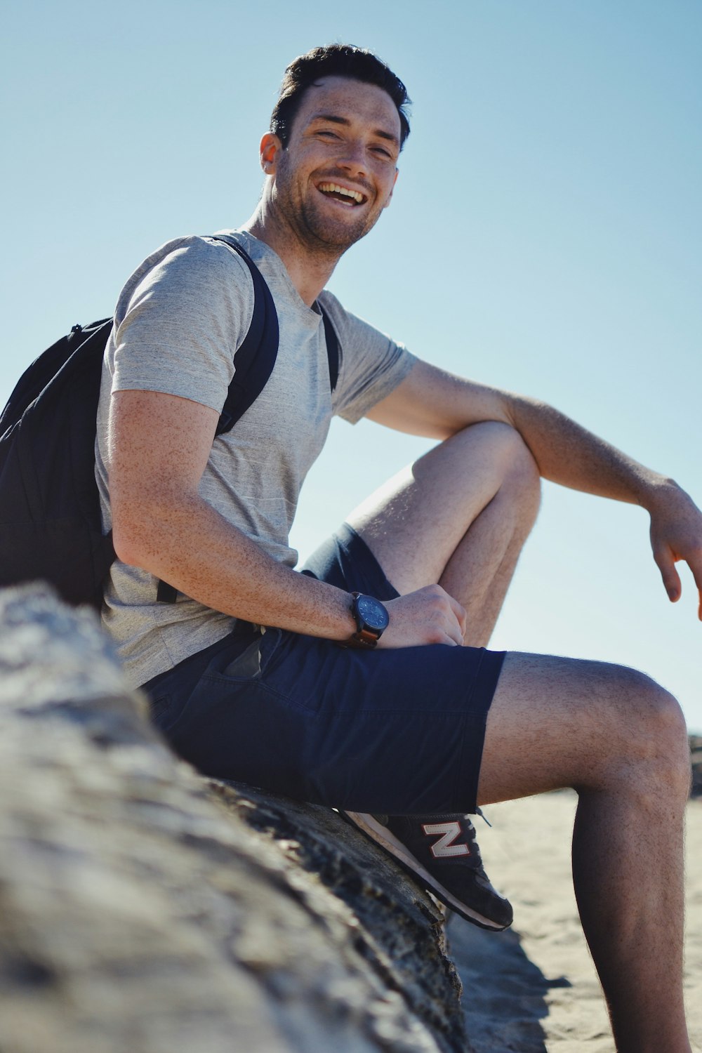 homme souriant assis sur la roche grise pendant la journée