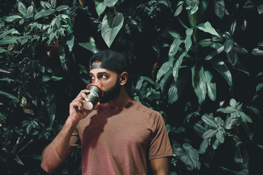 man drinking behind green leafed plnats