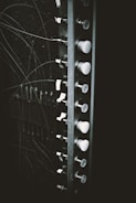 A section of an old electrical panel is visible, featuring a series of switches or knobs aligned vertically. The panel is surrounded by numerous thin wires that appear to be tangled. The image gives a vintage, industrial feel due to the black and white color scheme.