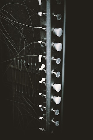A section of an old electrical panel is visible, featuring a series of switches or knobs aligned vertically. The panel is surrounded by numerous thin wires that appear to be tangled. The image gives a vintage, industrial feel due to the black and white color scheme.