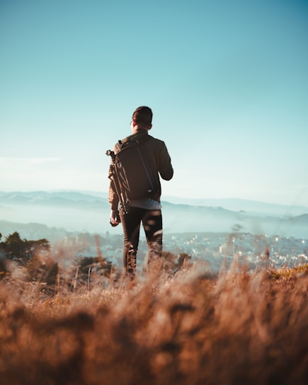 man standing on dried grass field while watching aerial view of village at daytime
