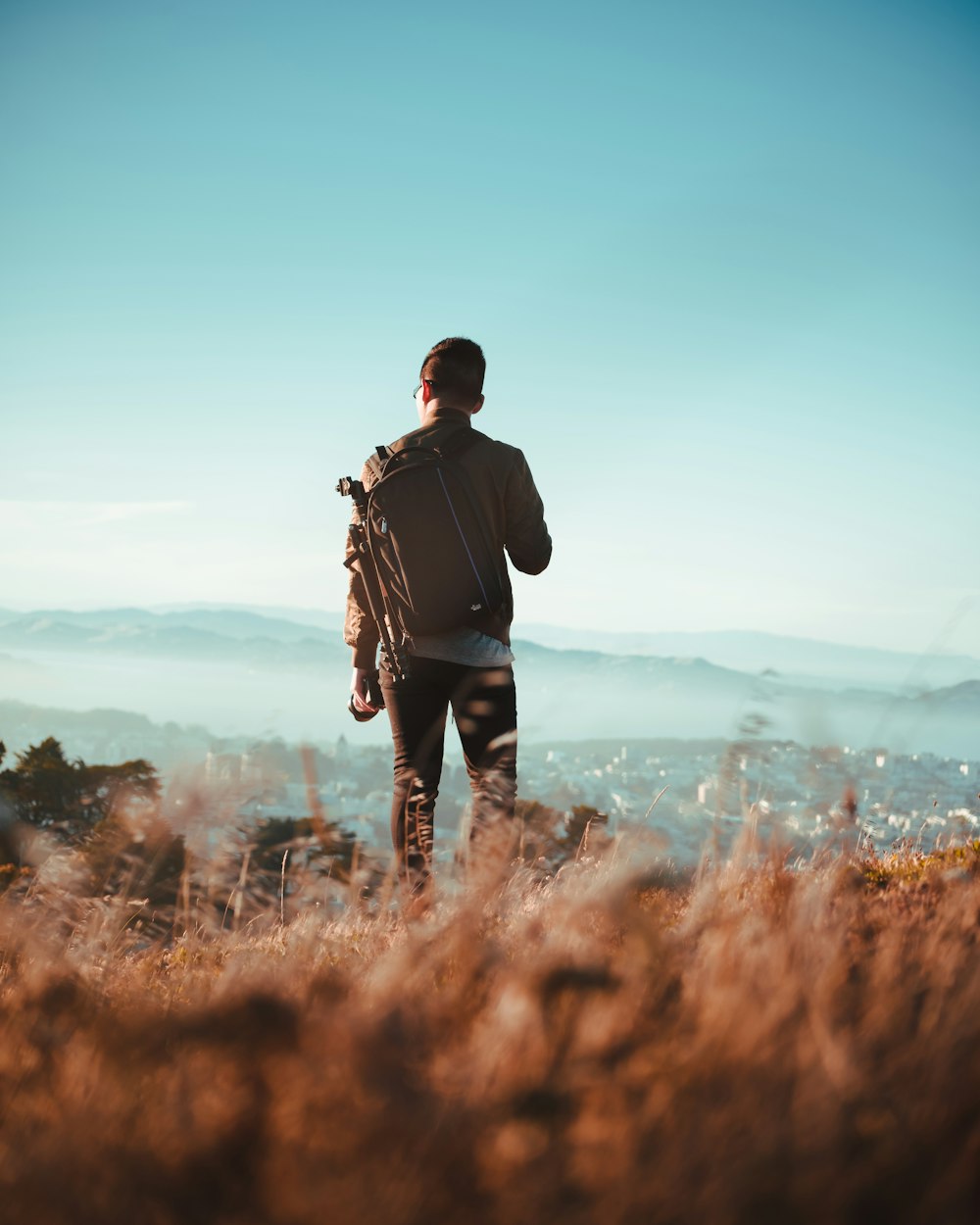 man standing on dried grass field while watching aerial view of village at daytime