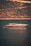 A luxurious yacht is floating on calm waters with a backdrop of a steep, wooded hillside. The light creates a golden reflection on the water.