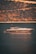 A luxurious yacht is floating on calm waters with a backdrop of a steep, wooded hillside. The light creates a golden reflection on the water.