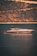 A luxurious yacht is floating on calm waters with a backdrop of a steep, wooded hillside. The light creates a golden reflection on the water.