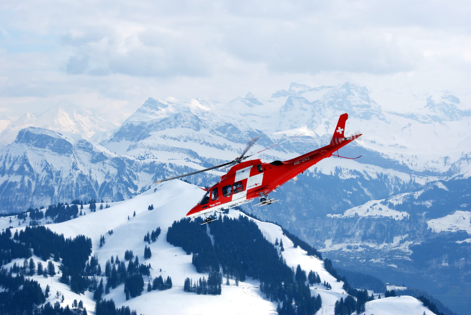 Hélicoptère de sauvetage rouge et blanc au-dessus de montagnes enneigées — photo d'illustration prise en Suisse centrale, non prise à Vallorcine