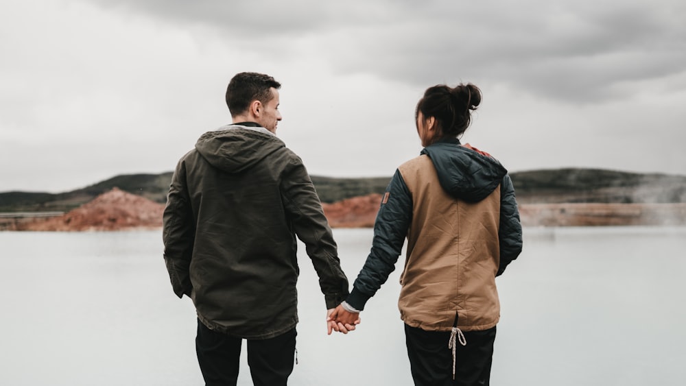 pareja que se toma de la mano frente al cuerpo de agua tranquila con la distancia de la montaña