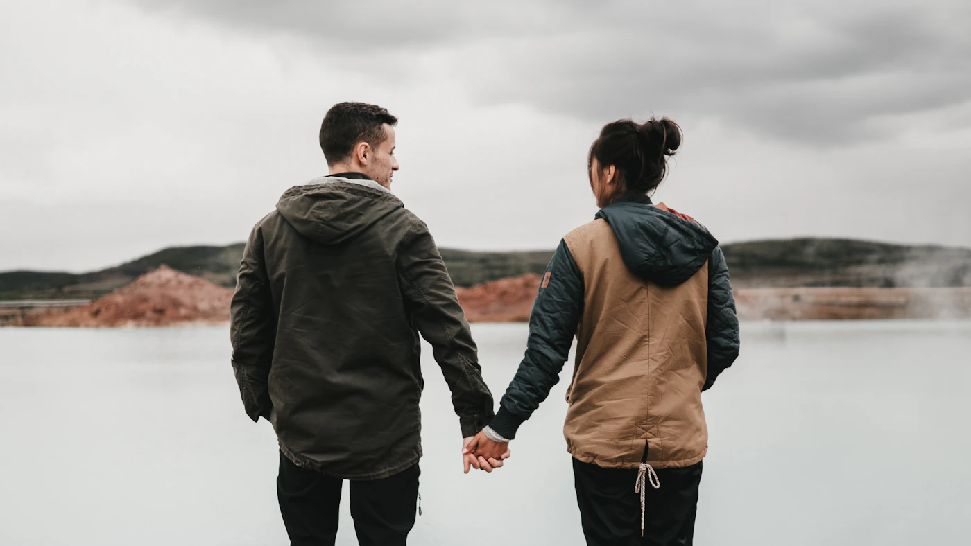 Couple holding hands beside calm water and mountains