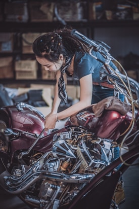 A person is working on a motorcycle in a garage environment, focusing on repairing or adjusting the vehicle. The scene includes various mechanical tools and motorcycle parts, and the person appears to be deeply engaged in their task.