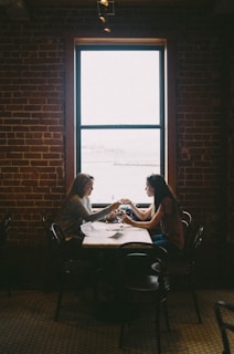 woman sitting in front of woman near window