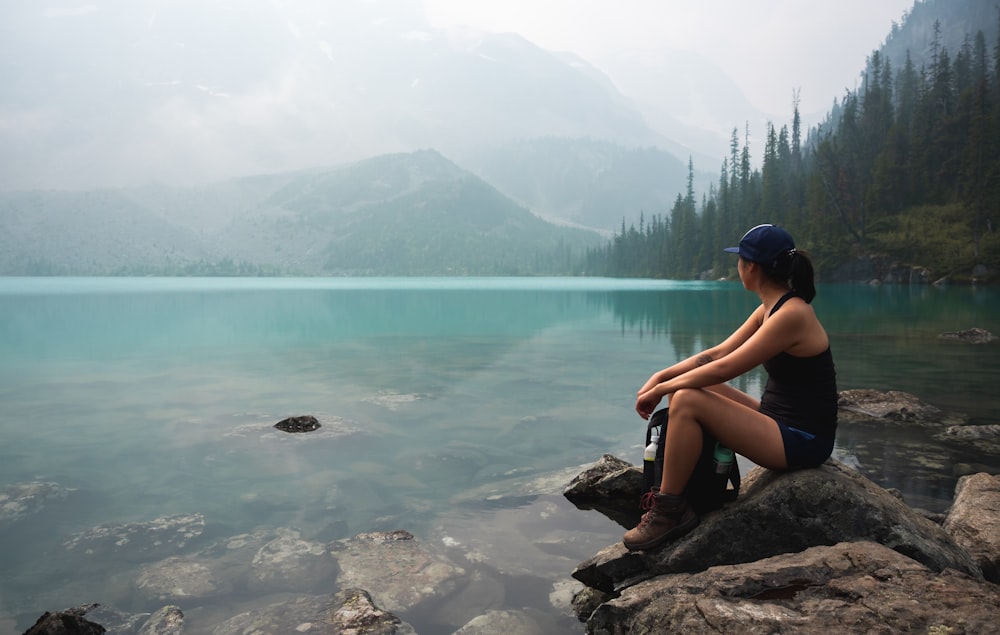 woman sitting on rock near body of water