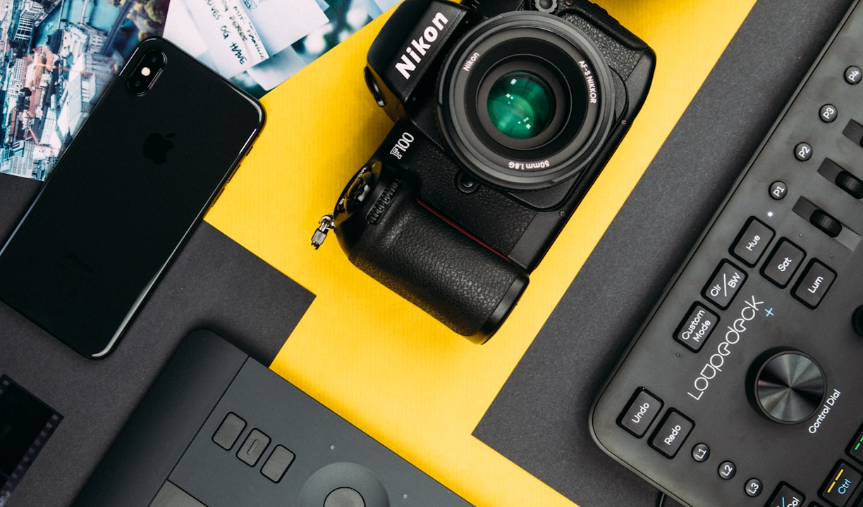 black Nikon DSLR camera beside space gray iPhone X