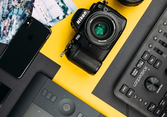 black Nikon DSLR camera beside space gray iPhone X