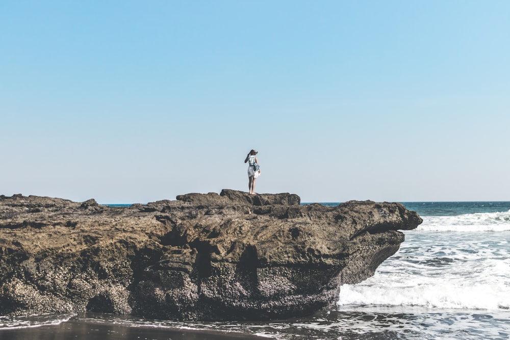 person standing on top of rock formation beside body of water