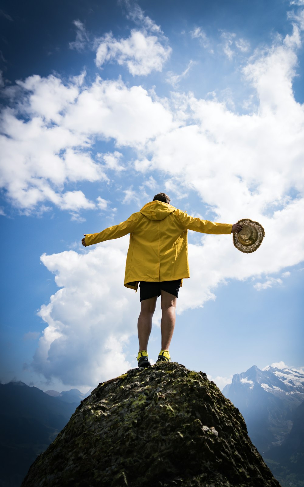 man holding brown strawhat standing on top of rock