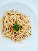 Close-up of a steaming plate of creamy carbonara pasta garnished with fresh parsley.