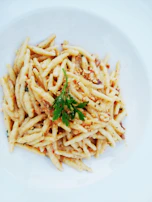 A chef sprinkling fresh herbs over a steaming plate of pasta.