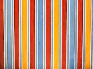 Vertical stripes in a repeating pattern with alternating colors of red, blue, yellow, and white. The stripes are evenly spaced and of consistent width, creating a rhythmic and vibrant pattern.