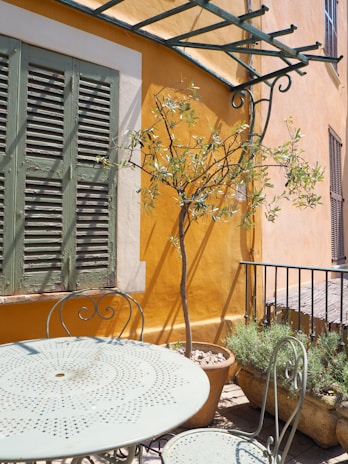 Sunlit outdoor patio with olive green cushions and beige curtains fluttering gently.