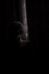 A shadowy figure lurking behind tattered curtains in a dimly lit theatre room.