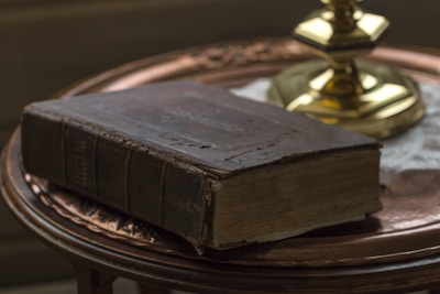 A close-up of a weathered leather-bound book resting on a wooden table, candlelight flickering nearby.