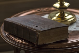 A close-up of a weathered leather-bound book resting on a wooden table, candlelight flickering nearby.