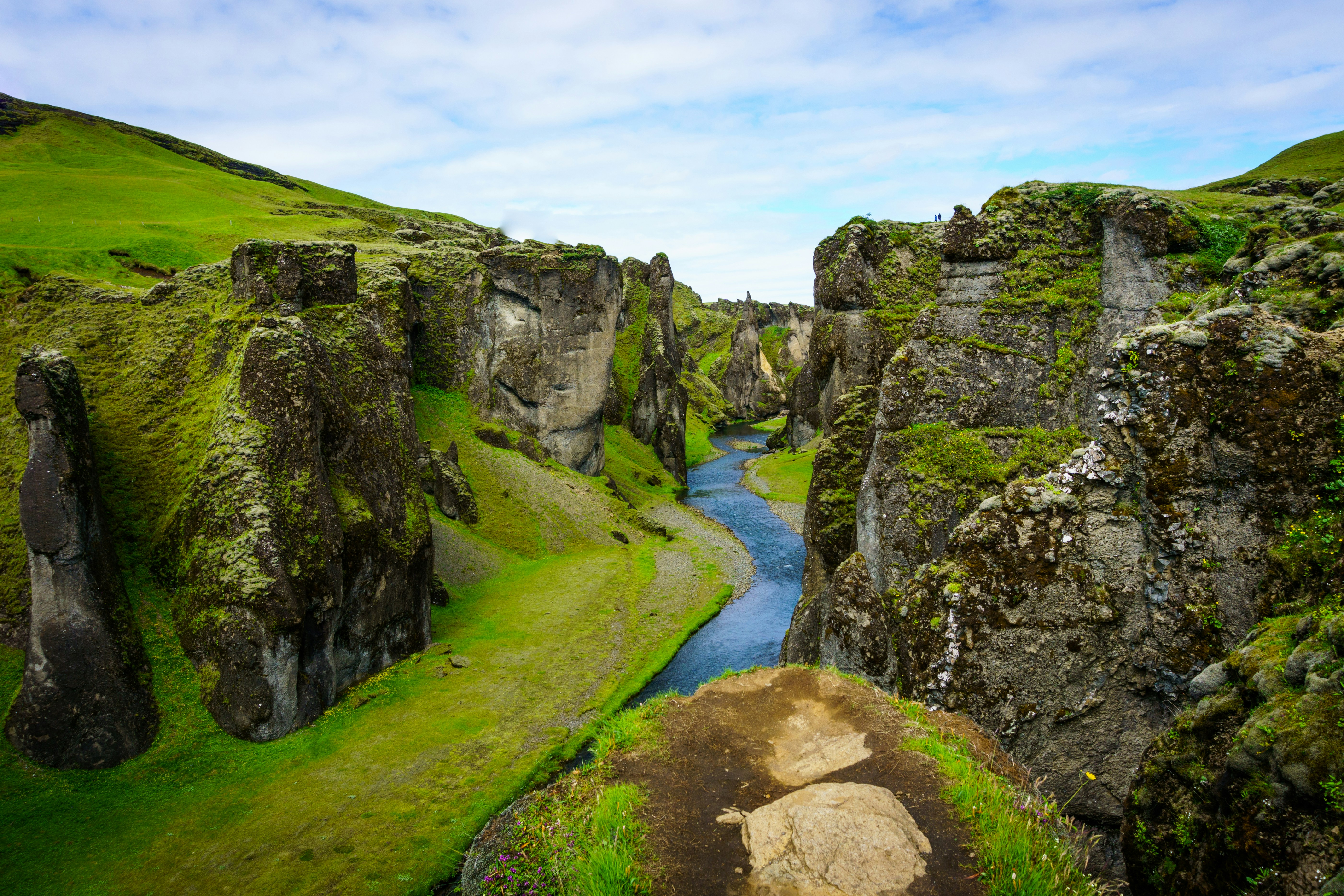 A winding blue river cuts through steep moss-covered cliffs in Fjaðrárgljúfur canyon, Iceland.