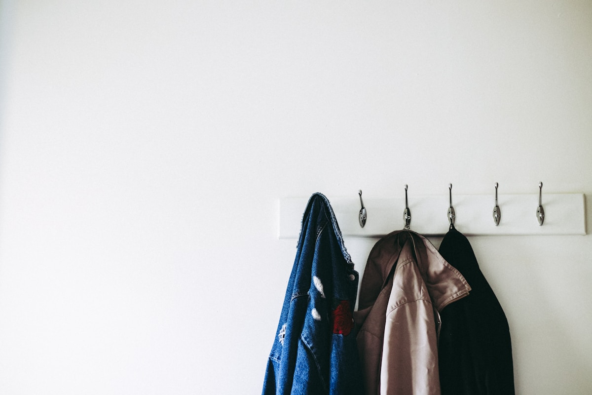 White wall-mounted hook rack with three jackets hanging near apartment entryway door